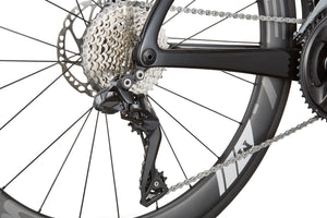 Close-up of EVOLUZIONE 1s rear derailleur and cassette, highlighting gears and chain on a black wheel with an aerodynamic design.