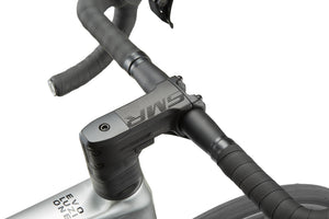 Close-up of a sleek road bike handlebar and stem with black tape and branding, hinting at the Masi EVOLUZIONE 1s metallic silver frame.