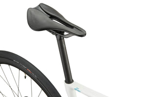 Close-up of black saddle and seatpost on a white GRAN CORSA road bike, with part of the rear wheel visible.