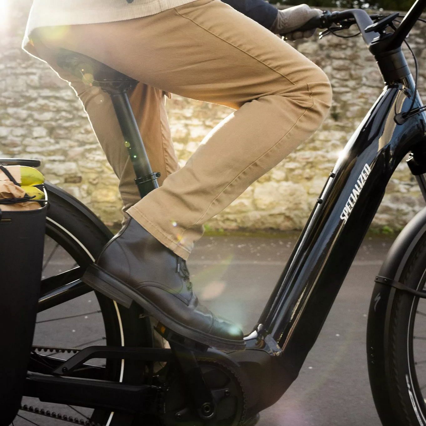 Person riding a black Specialized electric bike with a basket against a stone wall background